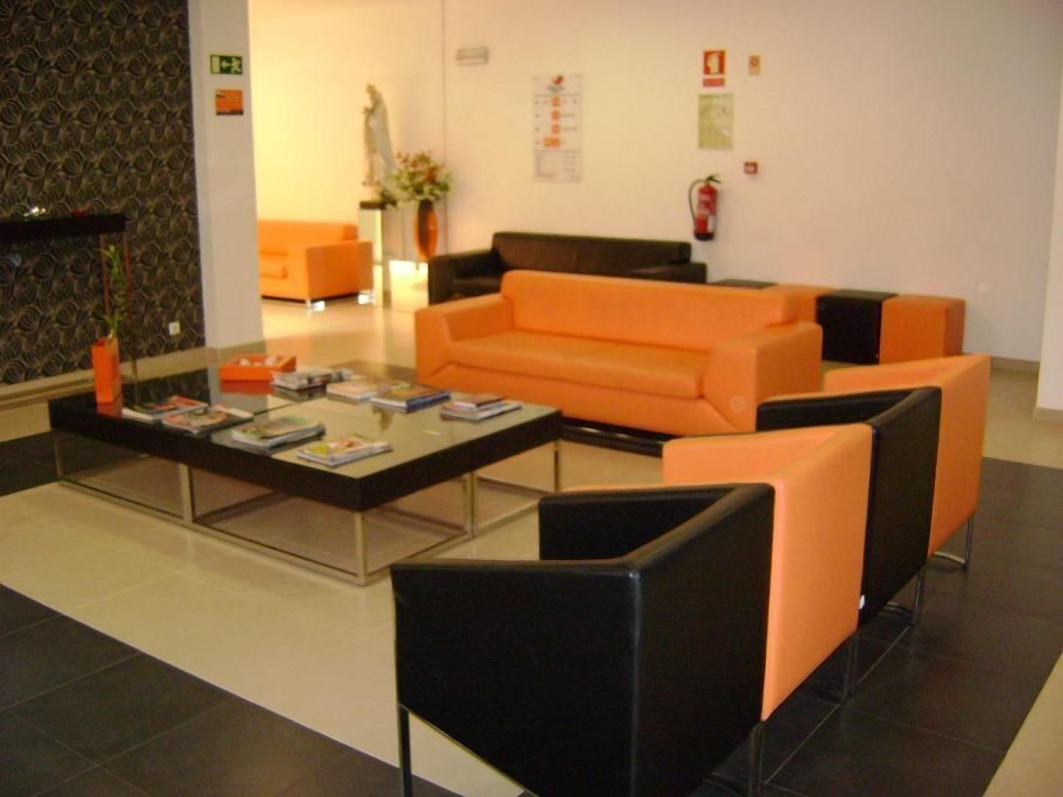 Un vestíbulo moderno con asientos naranja y negro, una mesa de centro de vidrio y un jarrón con flores.