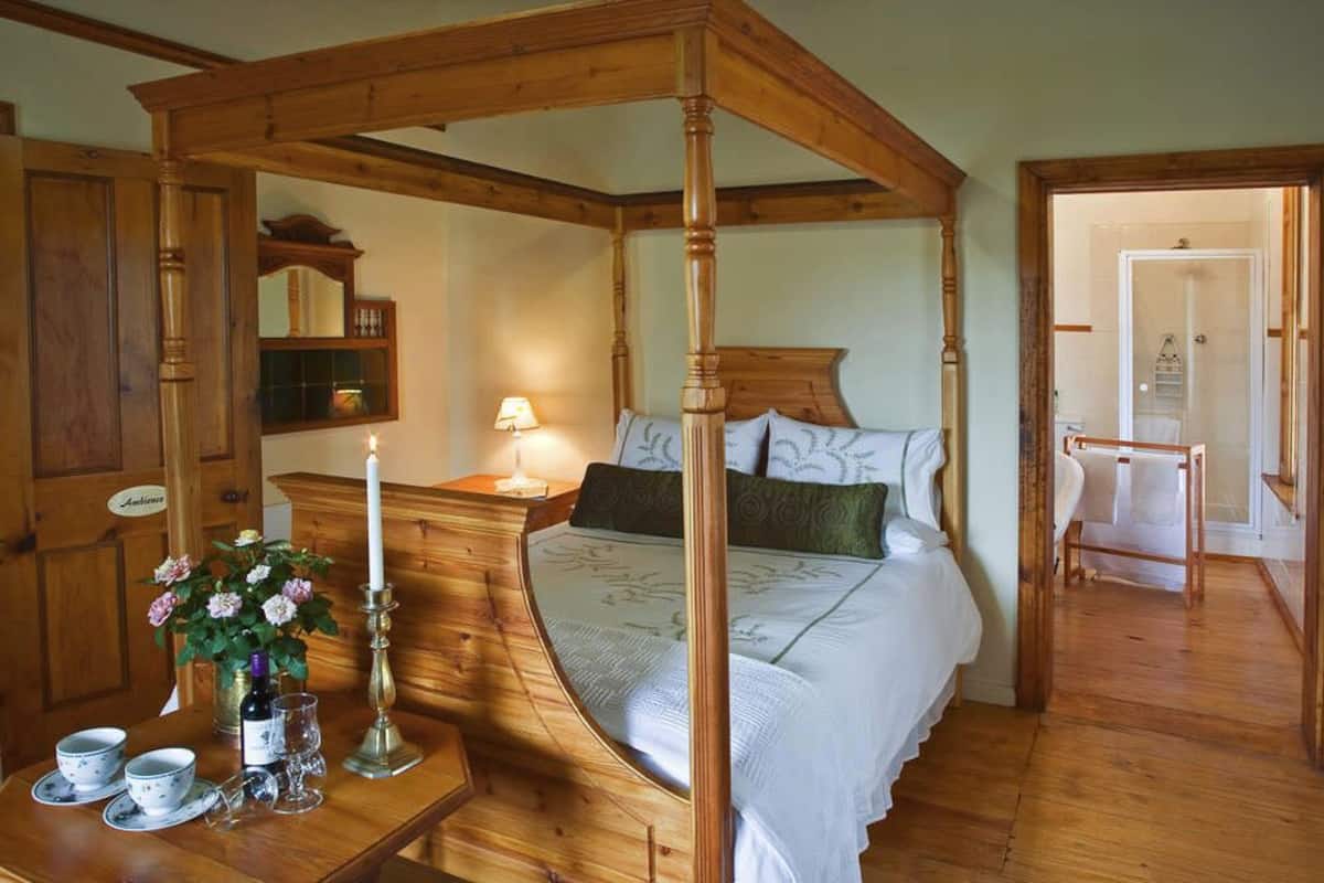 A four-poster bed with a wooden canopy, a bedside table with a lamp, and a mirror.
