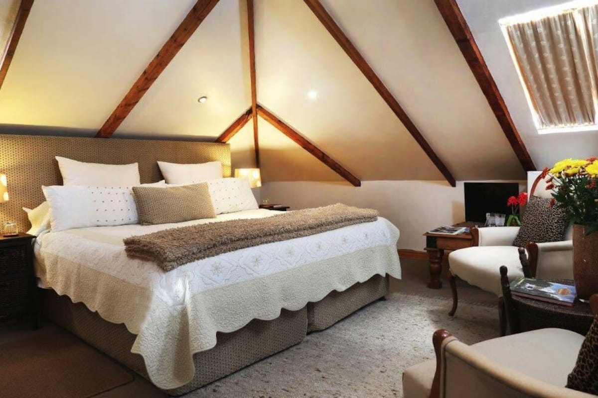 A bedroom with a large bed, a wooden ceiling, a nightstand, a chair, and a window with curtains.