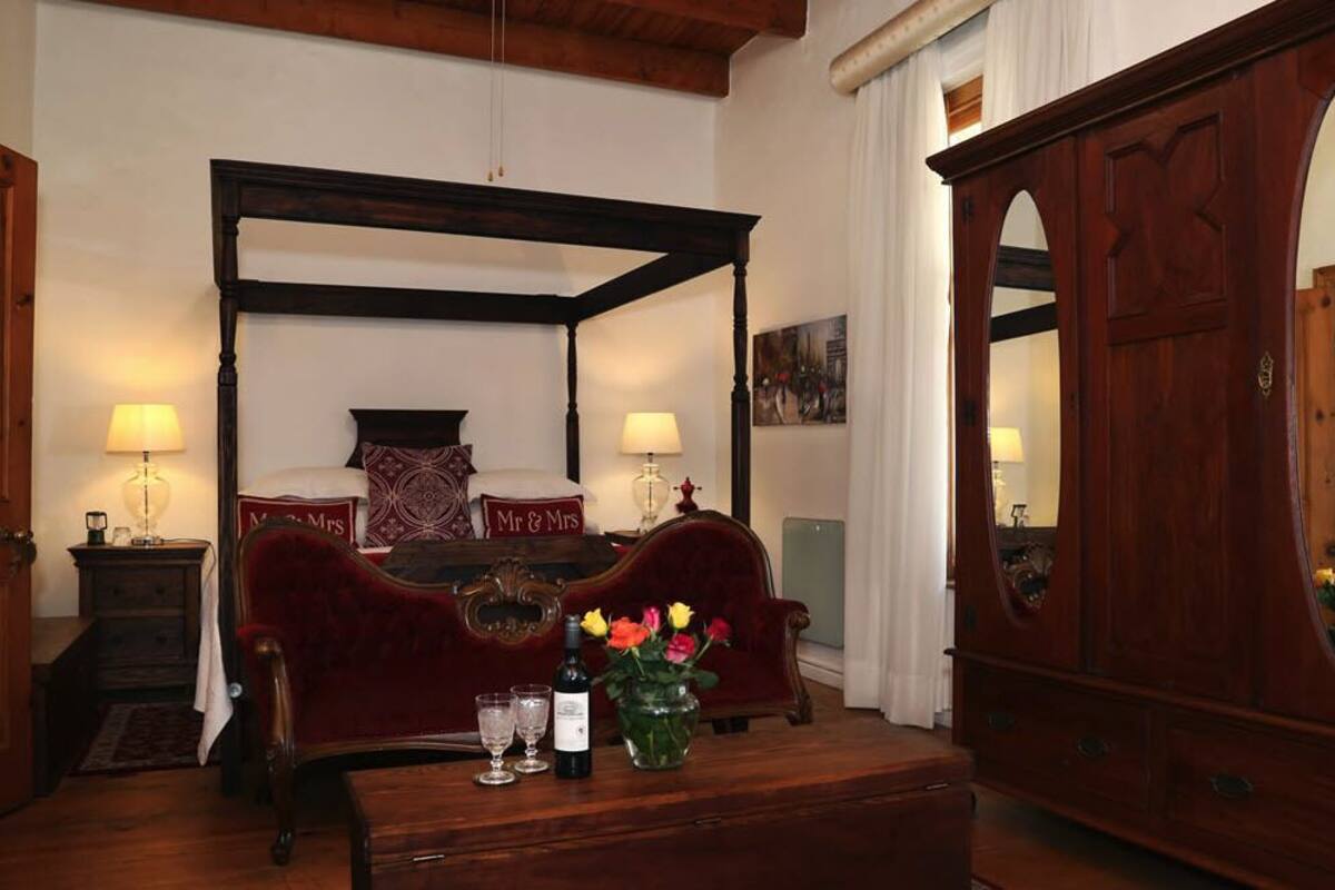 A traditional four-poster bed with matching pillows, a wooden nightstand, a mirror, and a vase with flowers.