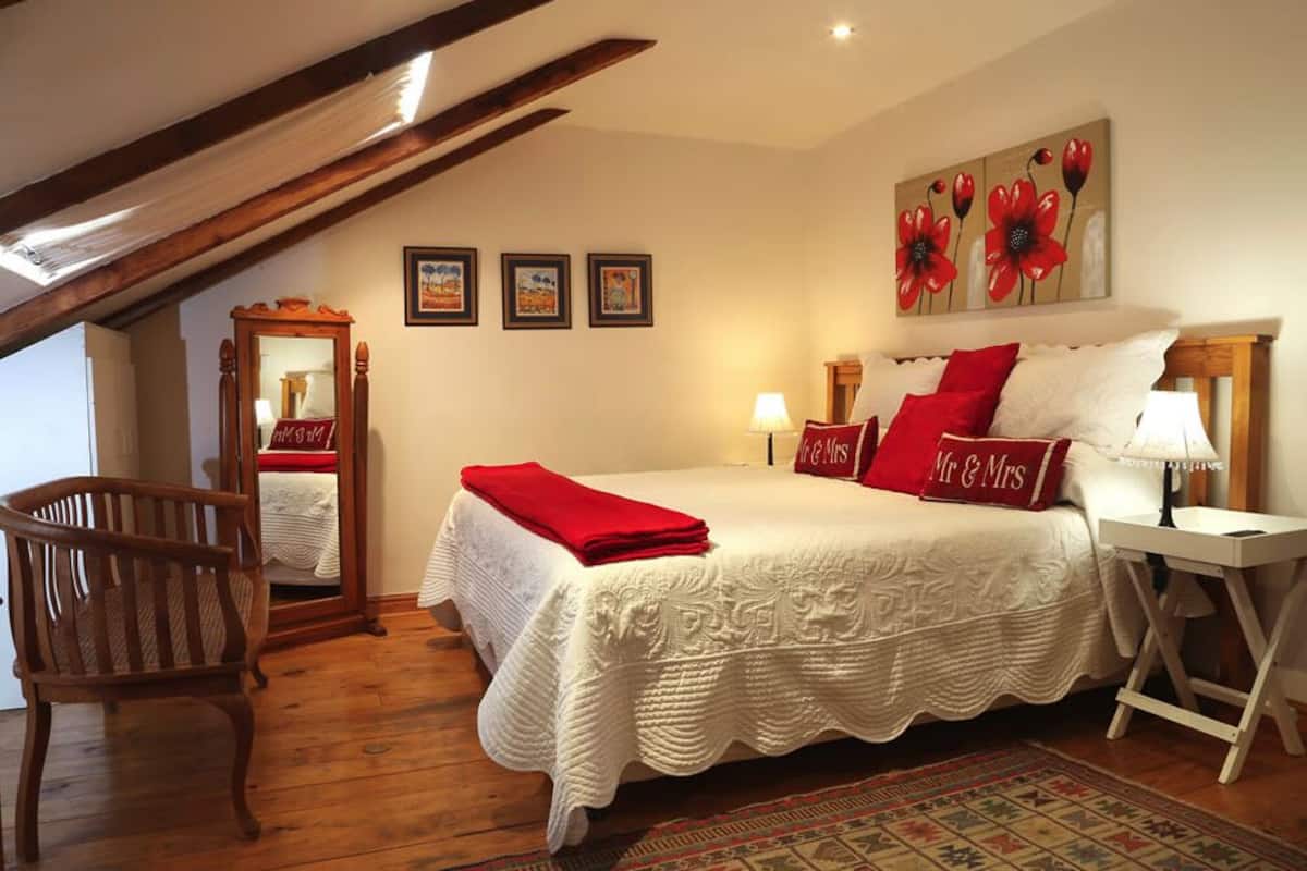 A bedroom with a bed, a chair, a nightstand, a lamp, and a mirror.