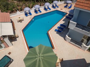 A swimming pool with blue water, surrounded by lounge chairs and umbrellas. - Athena Apartments (Hersonissos)