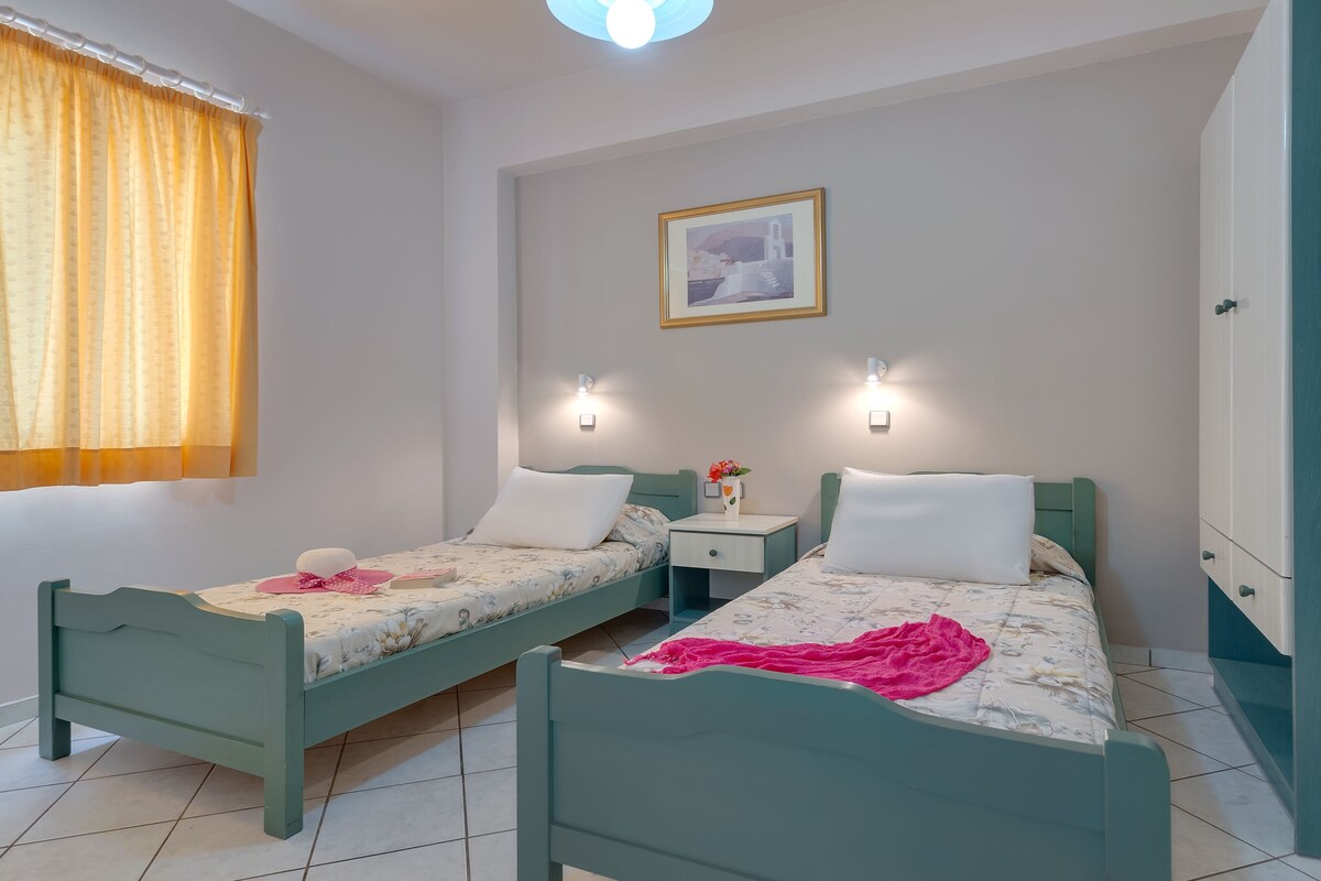 A twin room with two single beds, a nightstand, a wall-mounted light, a framed picture, and a window with curtains.