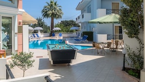 A pool area with lounge chairs, a foosball table, and a small table with a book. - Athena Apartments (Hersonissos)