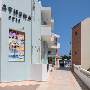 A building with a sign reading 'ATHENA APTS' and a poster advertising a swimming pool and snack bar. - Athena Apartments (Hersonissos)