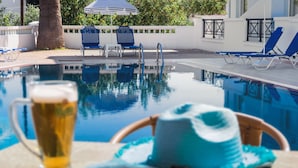 A poolside setting with a clear view of the pool, lounge chairs, and a beverage. - Athena Apartments (Hersonissos)
