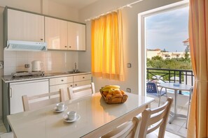 A modern kitchen with white cabinets, a coffee maker, and a dining area with a glass table and chairs. - Athena Apartments (Hersonissos)