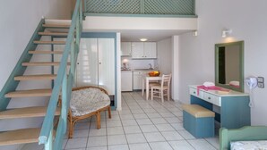 A room with a staircase, a dining area, a kitchenette, and a bed.