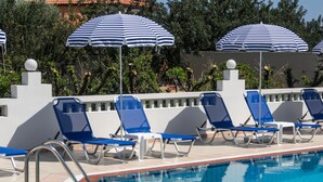 A swimming pool with blue and white striped umbrellas, blue lounge chairs, and a tiled deck.
