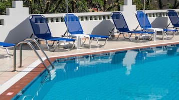 A swimming pool with blue and white striped umbrellas, blue lounge chairs, and a tiled deck.