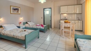 A room with two beds, a small kitchen, and a dining area.
