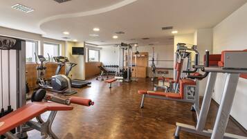 Un gimnasio con diverso equipo de ejercicio, suelo de madera y ventanas grandes.