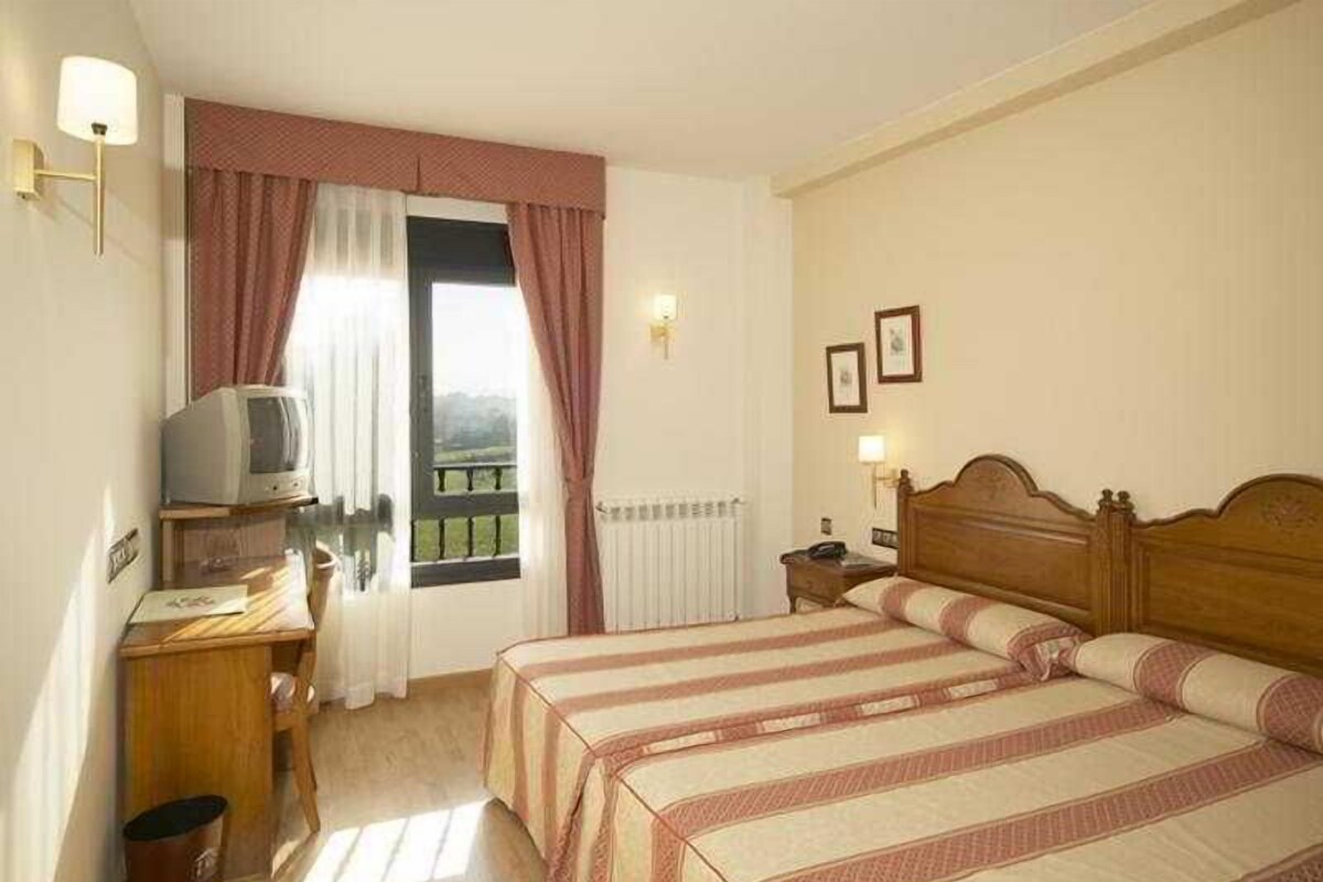 Ein Hotelzimmer mit Bett, Schreibtisch mit Fernseher, Fenster mit Vorhängen und Heizkörper.