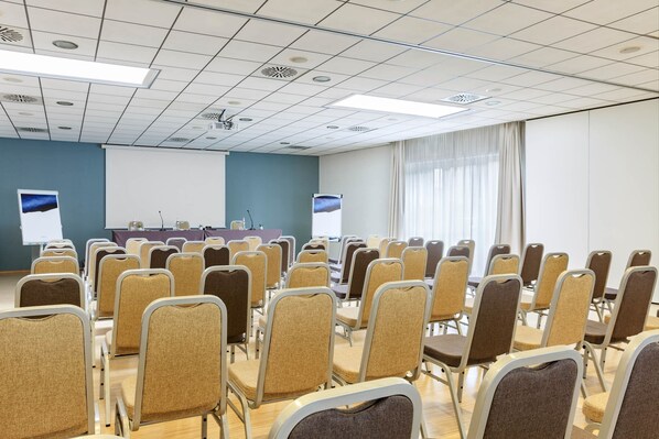 A conference room with rows of chairs, a projector screen, and a presentation area. - voco Venice Mestre - The Quid by IHG (Mestre)