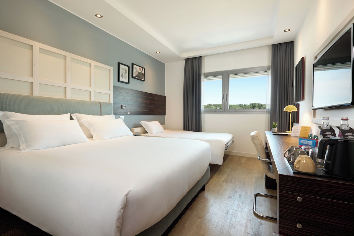 Une chambre d’hôtel avec deux lits, un bureau avec une machine à café, une télévision et une fenêtre donnant sur un paysage agréable.