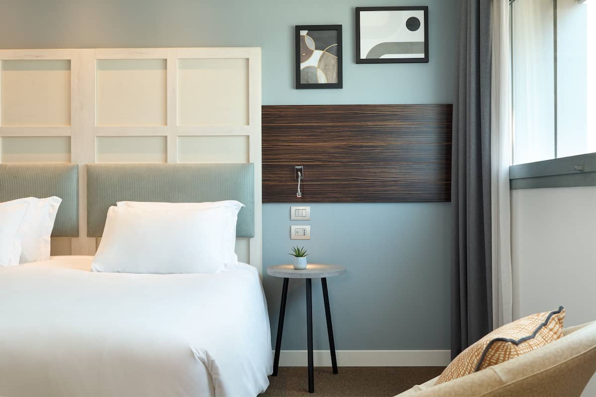 Een hotelkamer met een bed, een klein rond tafeltje met een plant en een hoofdbord met een houten paneel.