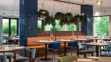 Ein modernes Restaurant mit runden Tischen, blauen Stühlen und hängenden Pflanzen.