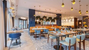 A modern restaurant with multiple dining areas, including a bar and a seating area with a high ceiling and pendant lighting. - voco Venice Mestre - The Quid by IHG (Mestre)