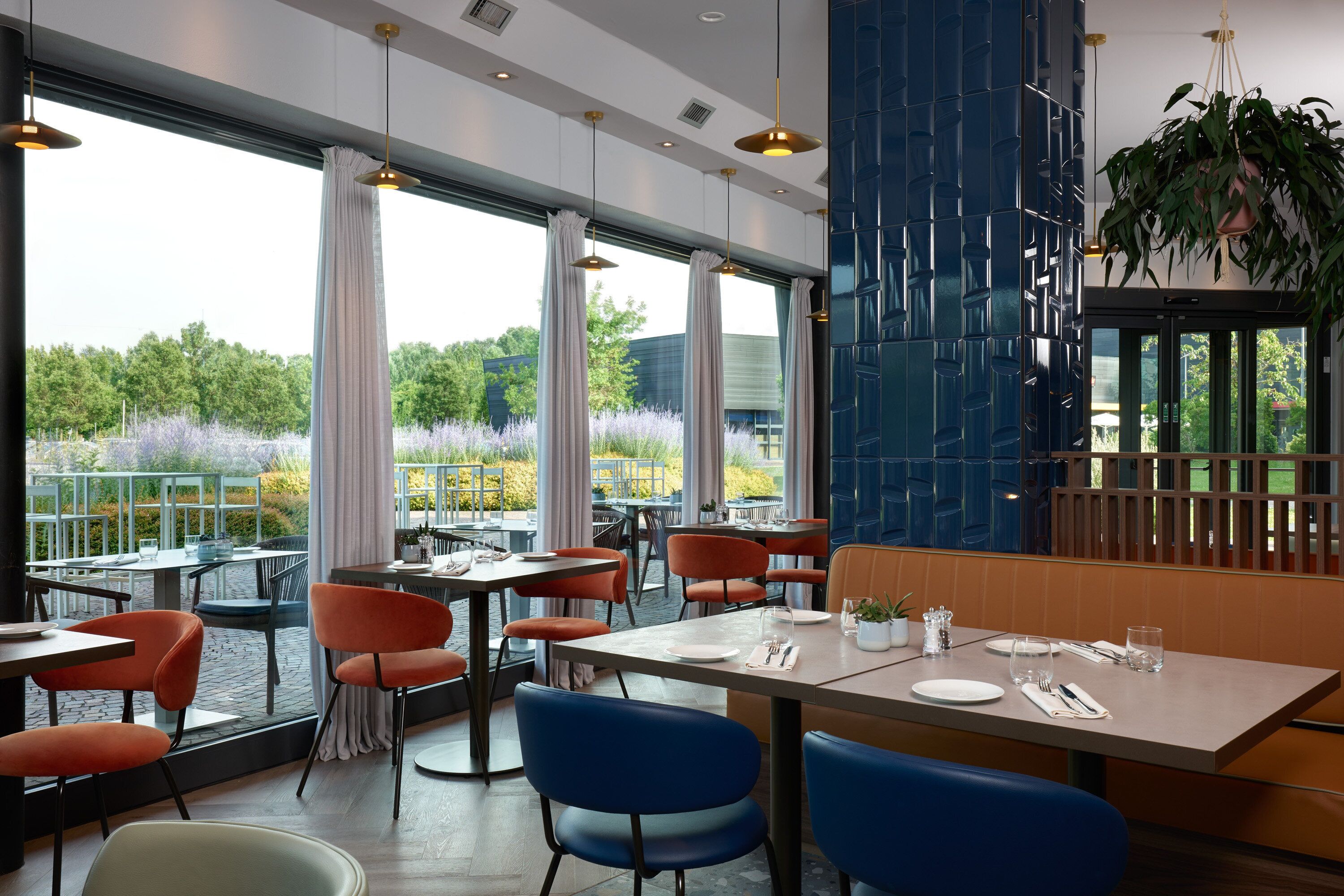 En restaurang med uteservering, stora fönster och utsikt över grönområden.