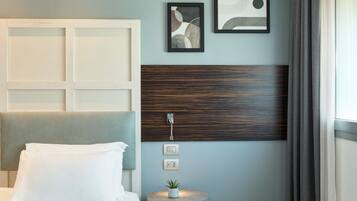 A hotel room with a bed, a small table with a plant, and a wall with two framed artworks.