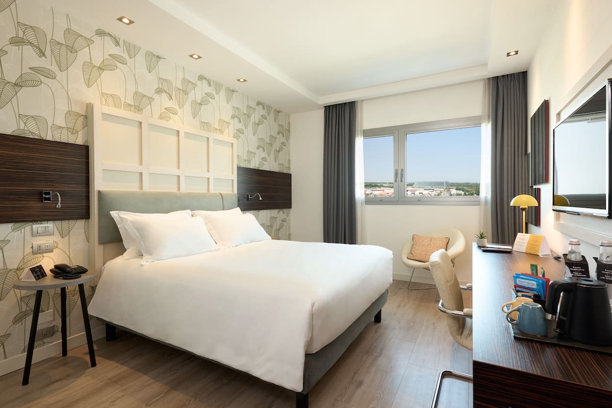 Een hotelkamer met een groot bed, een bureau met koffiezetapparaat, een stoel en uitzicht op de stad.