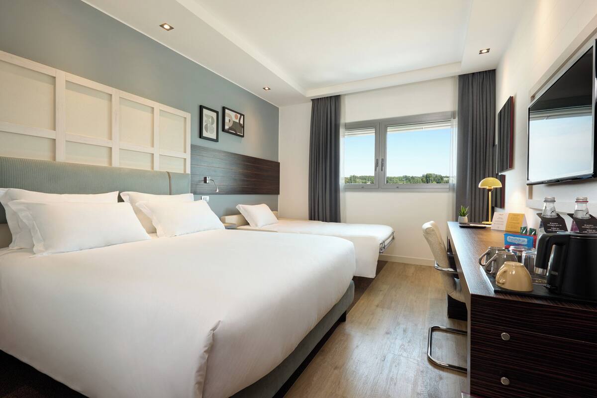 Een hotelkamer met twee bedden, een bureau met een koffiezetapparaat, een televisie en een raam met uitzicht.