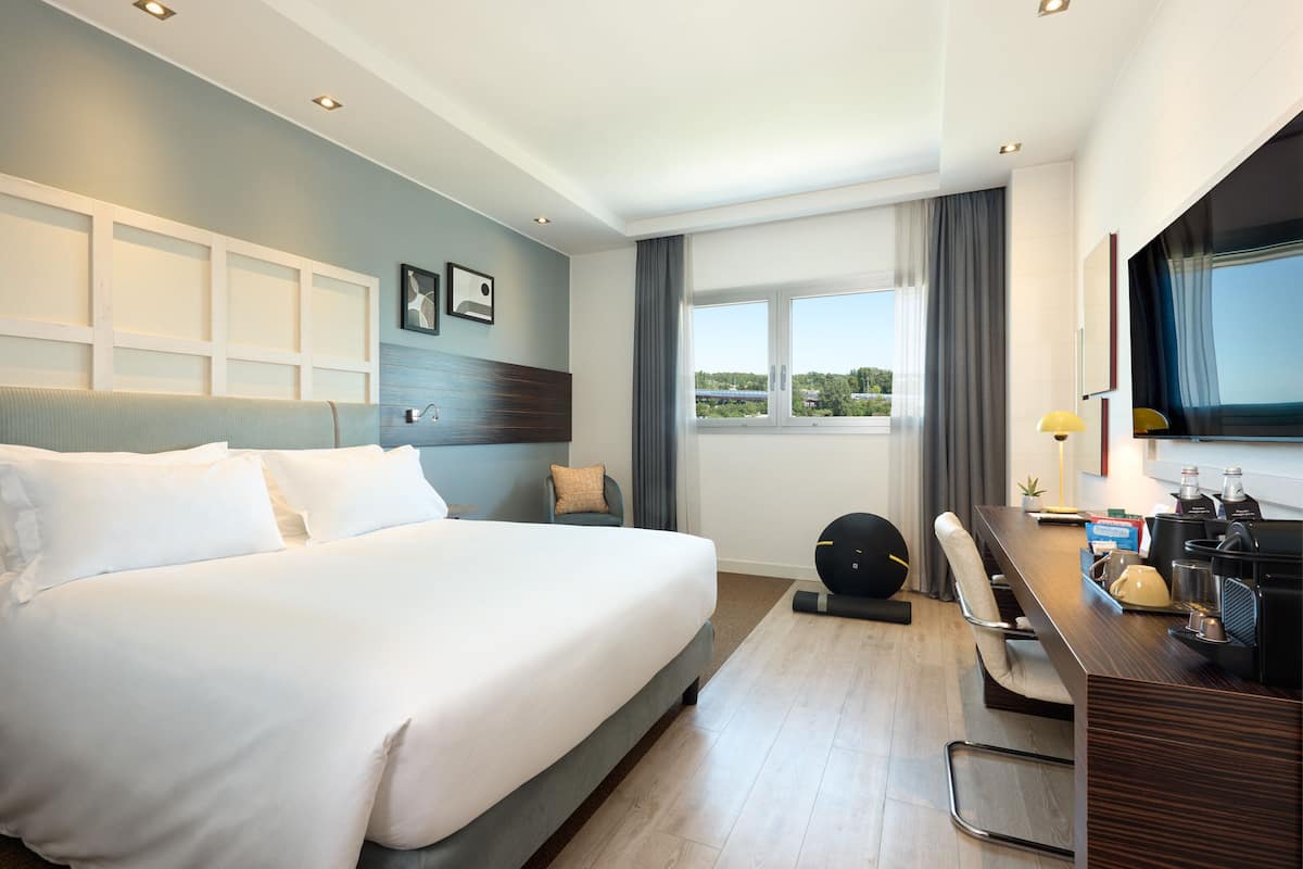 Une chambre d’hôtel moderne avec un grand lit, un bureau équipé d’un ordinateur et une vue sur l’extérieur.