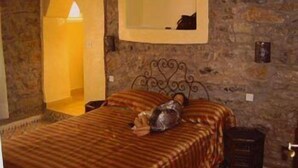 A bedroom with a stone wall, a bed with striped bedding, a bedside table, and a wall-mounted mirror. - Riad Dar Fatna (Ait Taguella)