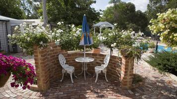 Un patio con pared de ladrillo, sillas de metal blanco, una mesita redonda y un paraguas azul.