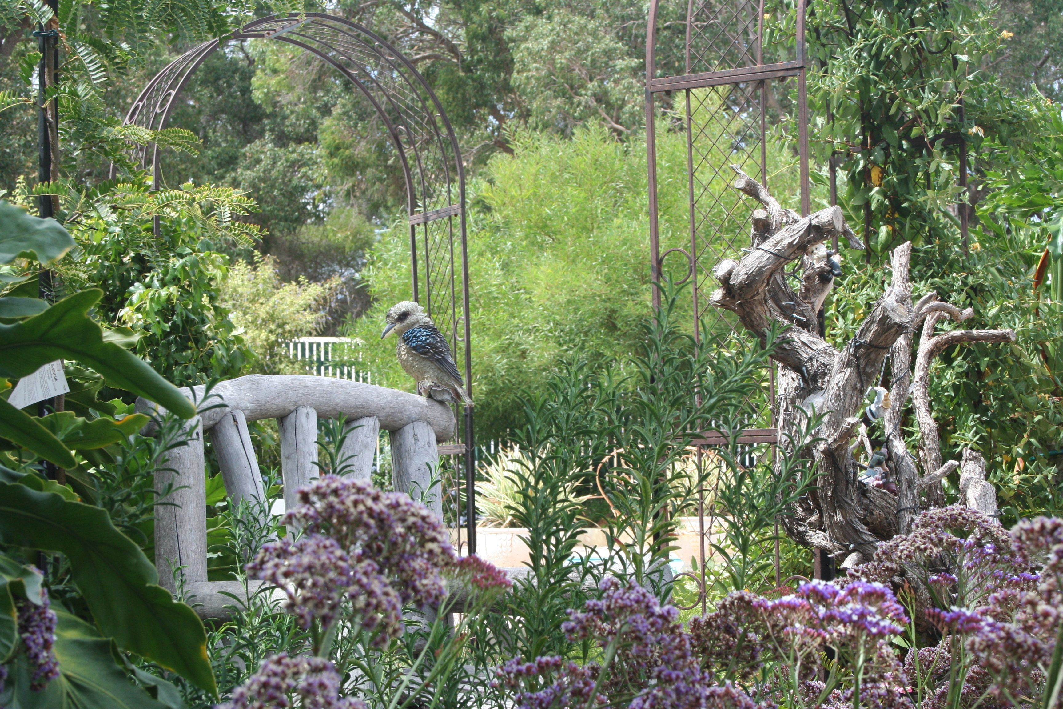 Un ave posada en una estructura de madera rodeada de vegetación exuberante y plantas con flores.
