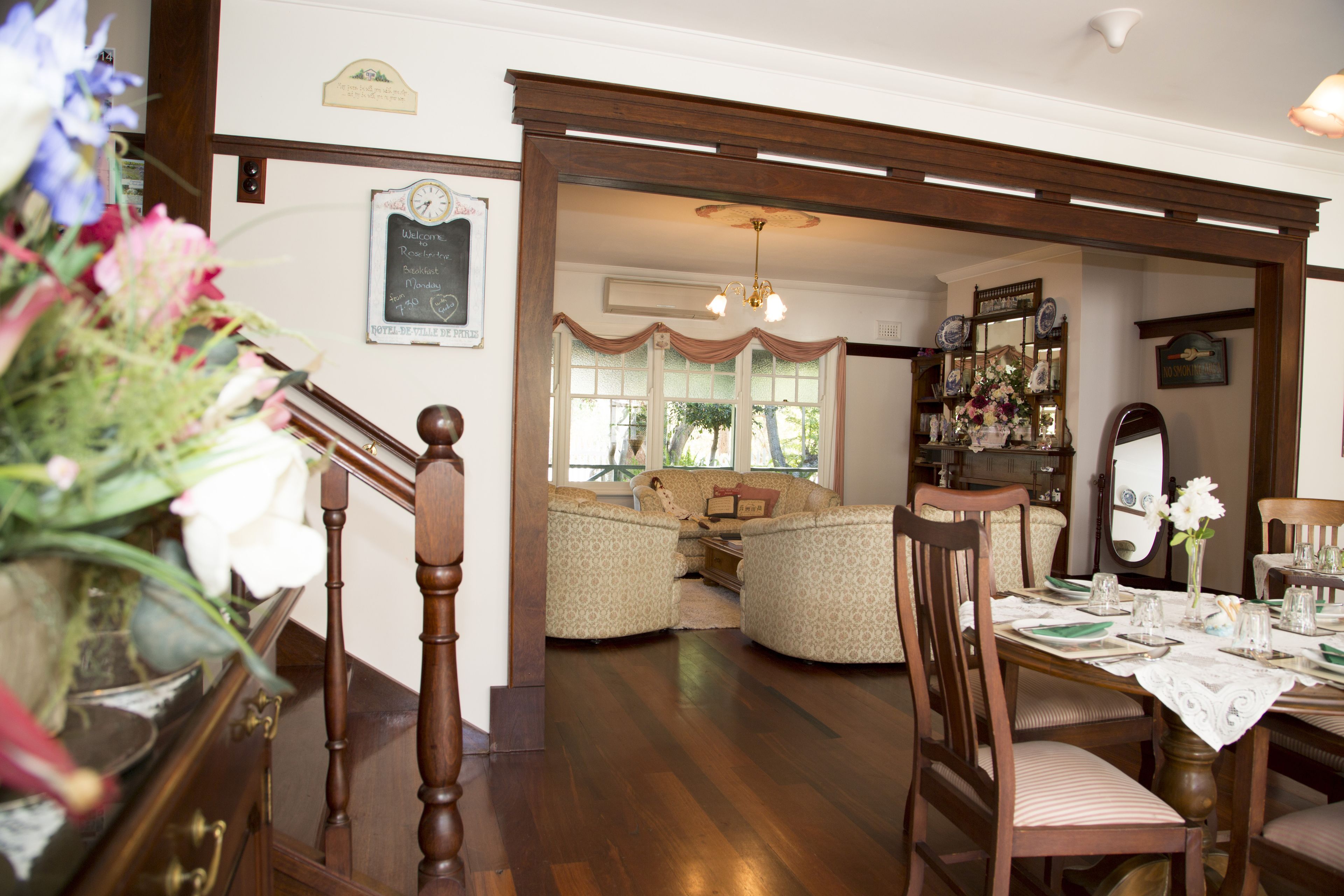 Un comedor con una mesa de madera dispuesta para cuatro, rodeada de sillas. Una escalera con barandilla de madera lleva a otra habitación.