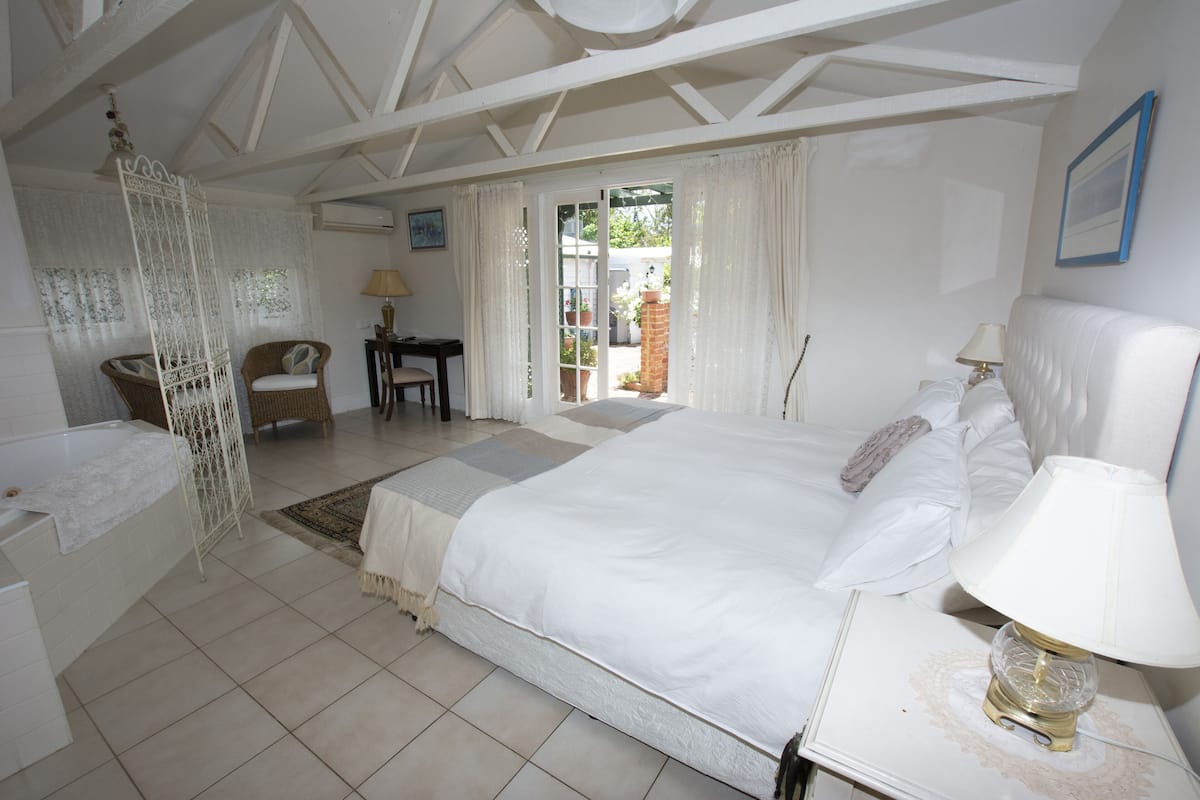 Quarto com uma cama grande, mesa de cabeceira com abajur, cadeira, escrivaninha e janela com cortinas.
