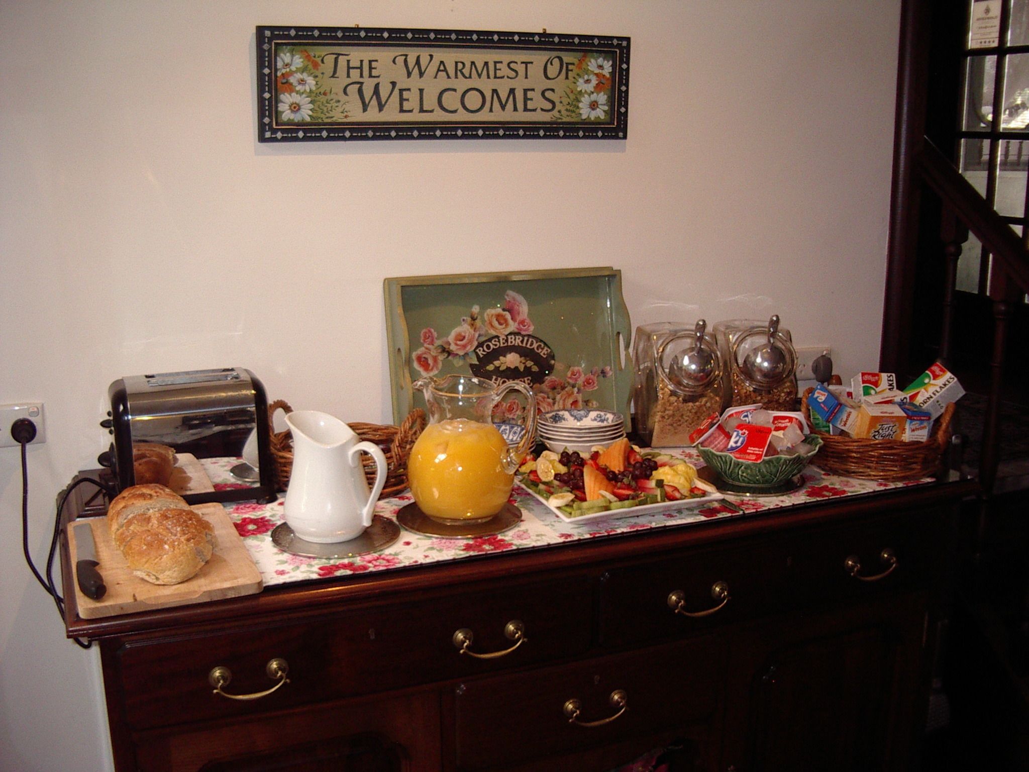 A breakfast setup with a toaster, bread, a pitcher of orange juice, and various breakfast items on a table.