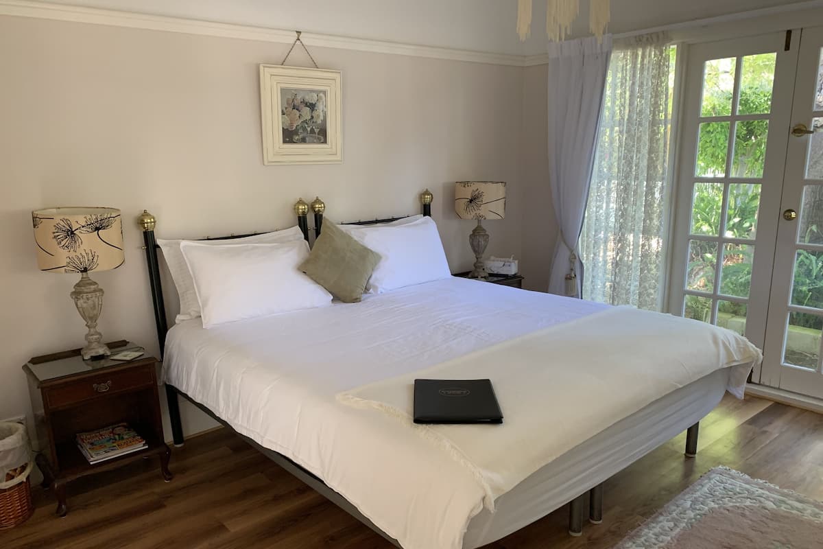 Uma cama bem arrumada com lençóis brancos, uma mesa de cabeceira com abajur e um quadro na parede.