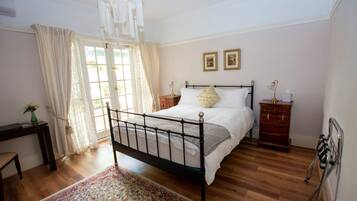 A bedroom with a bed, bedside tables, a chair, a desk, a window with curtains, and a chandelier.