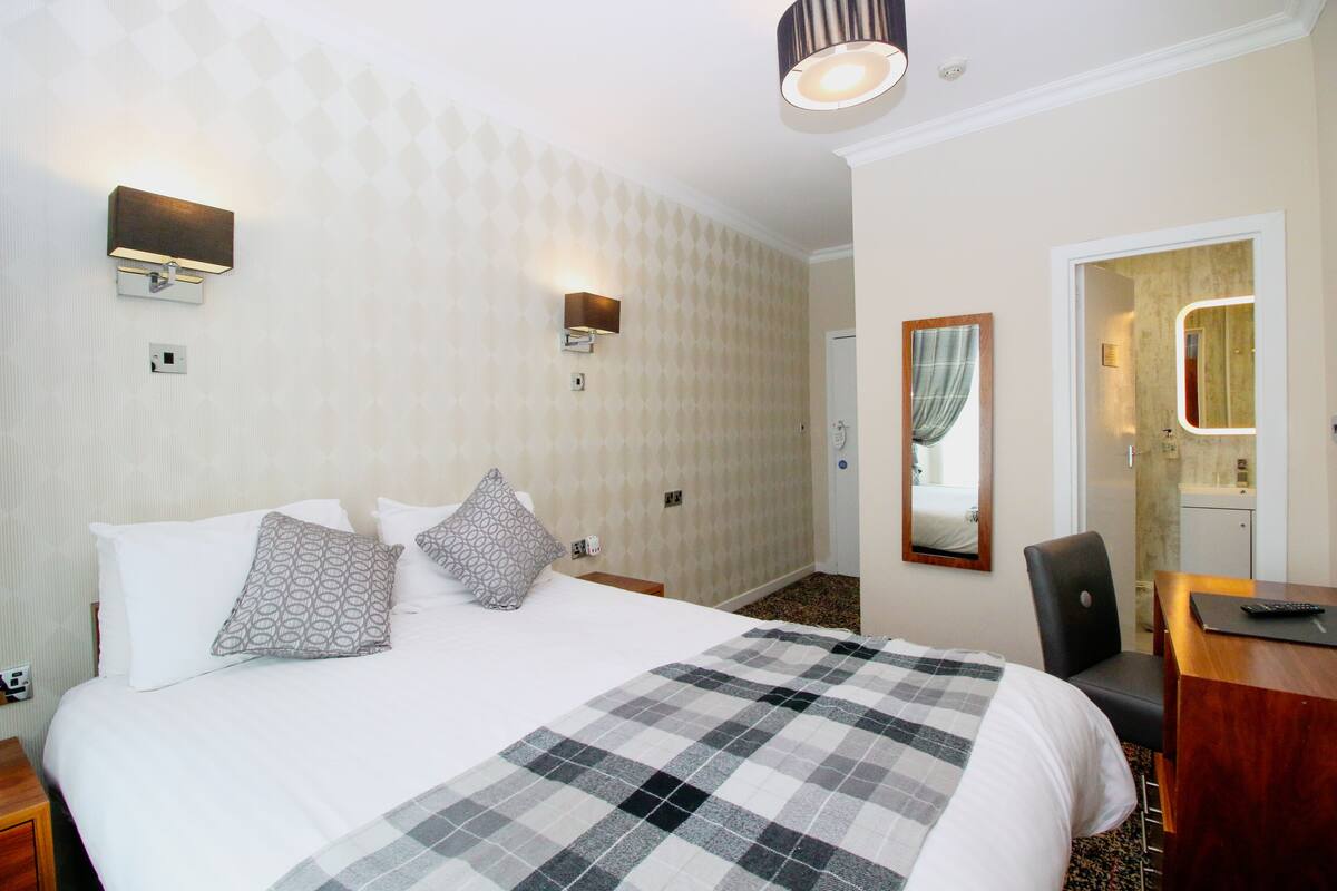 A hotel room with a large bed, two wall-mounted lights, a mirror, a desk, and a chair.
