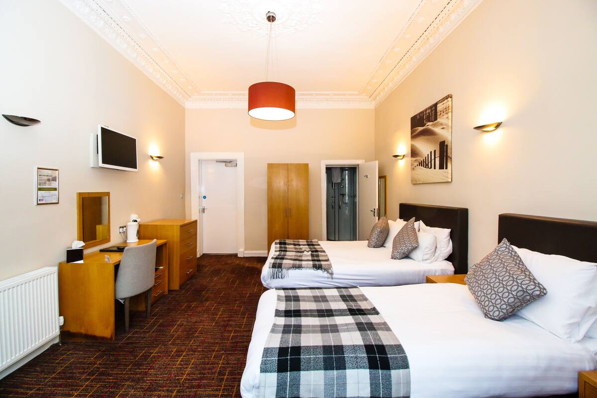 A hotel room with two beds, a desk, a chair, a television, and a red pendant light.