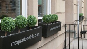 Een hotelschild, een rij zwarte plantenbakken met groen, en een websiteadres.