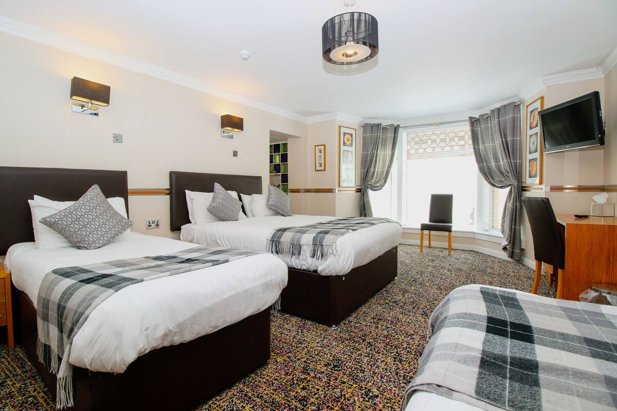 A hotel room with two beds, a desk, a TV, and a window with curtains.