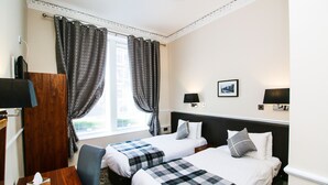 Een hotelkamer met twee bedden, een bureau, een stoel, een televisie en een raam met gordijnen.
