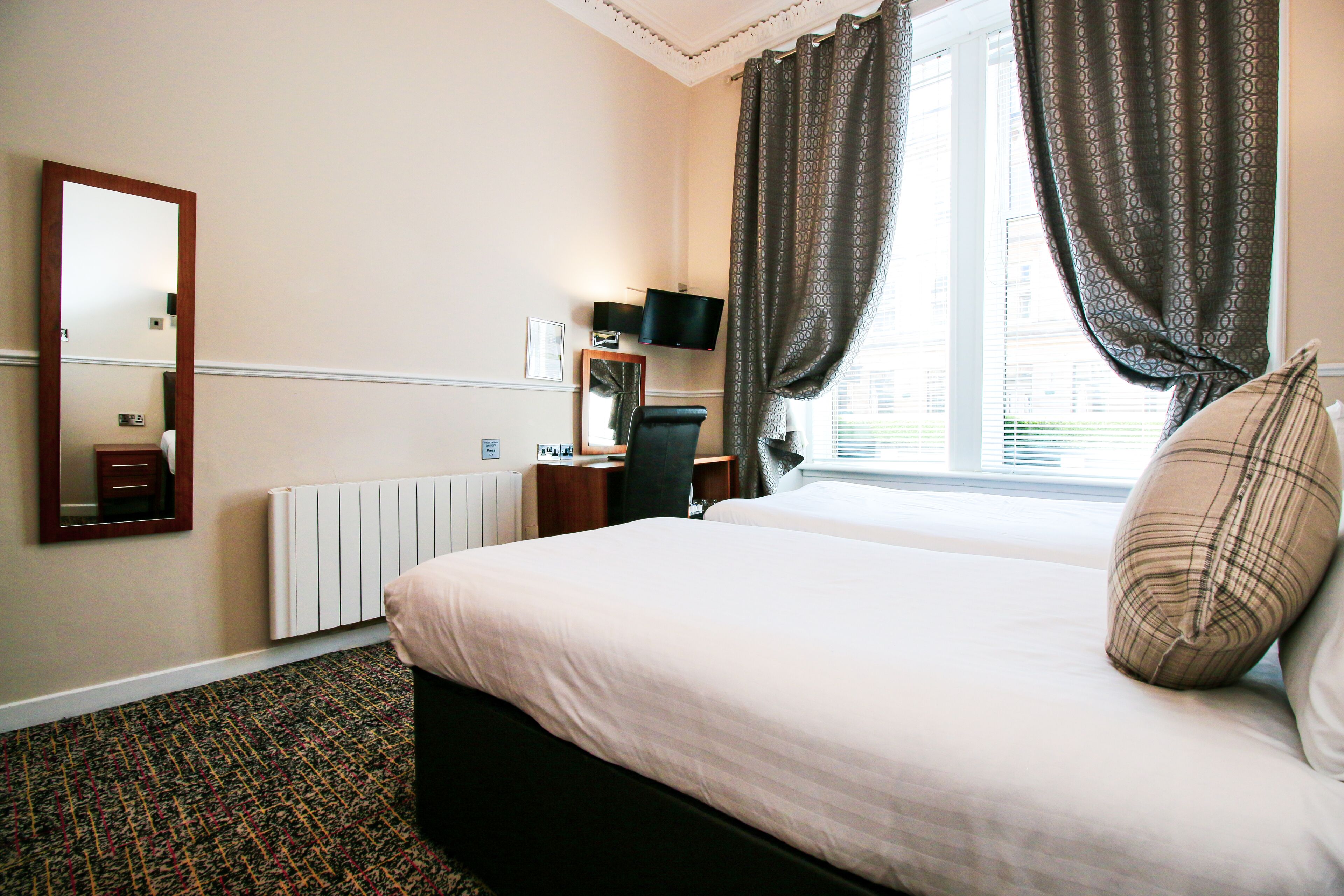 Hotelkamer met een bed, bureau, stoel, televisie en raam met gordijnen.