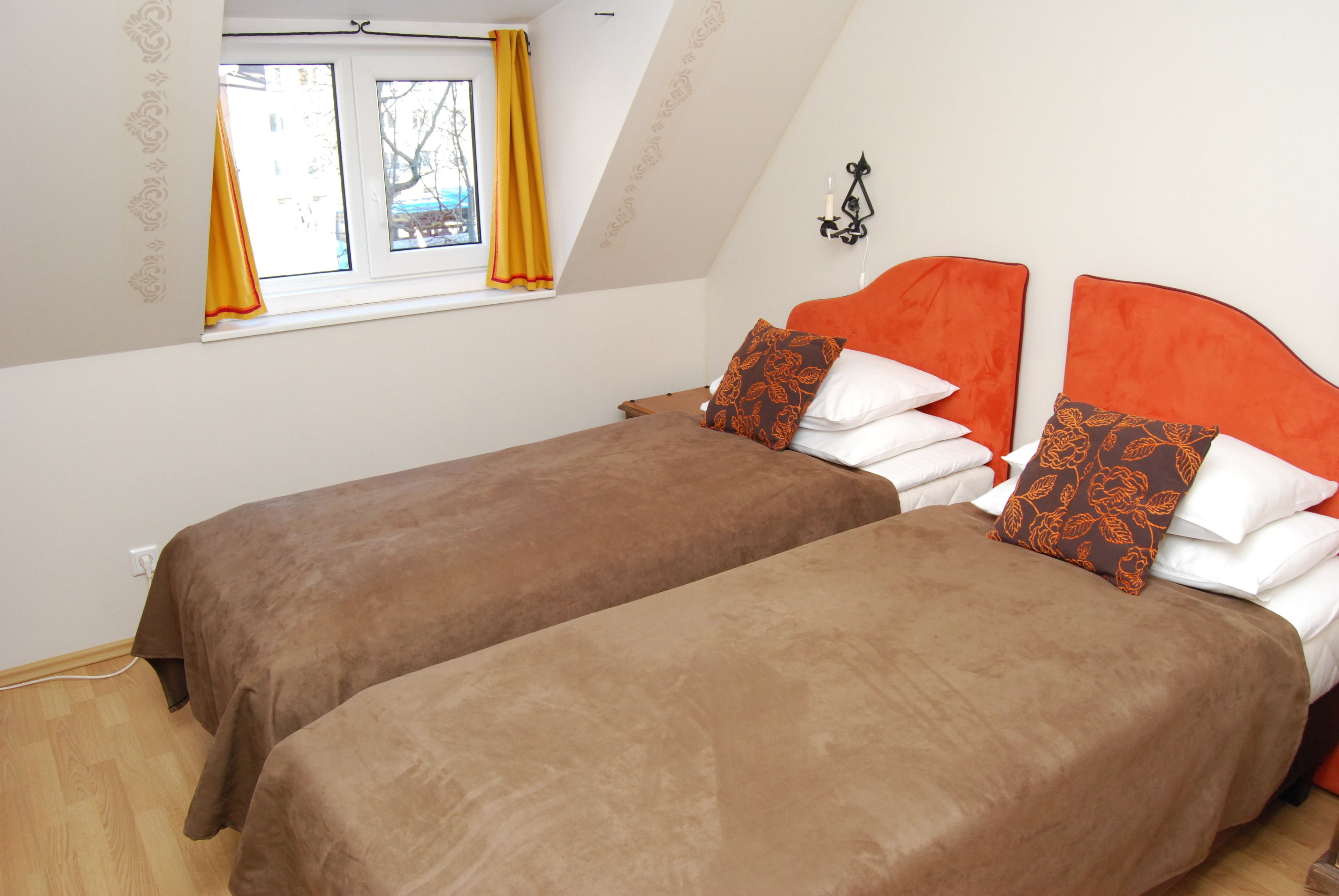 Un dormitorio con dos camas, una ventana con cortinas amarillas y una lámpara fijada a la pared.
