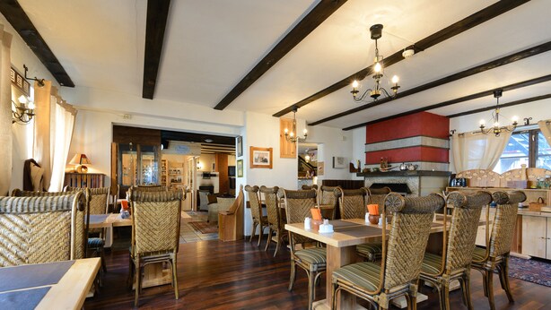 A dining area with wooden floors, wicker chairs, and a central table with candles. - Hotel Hansalinn (Parnu)