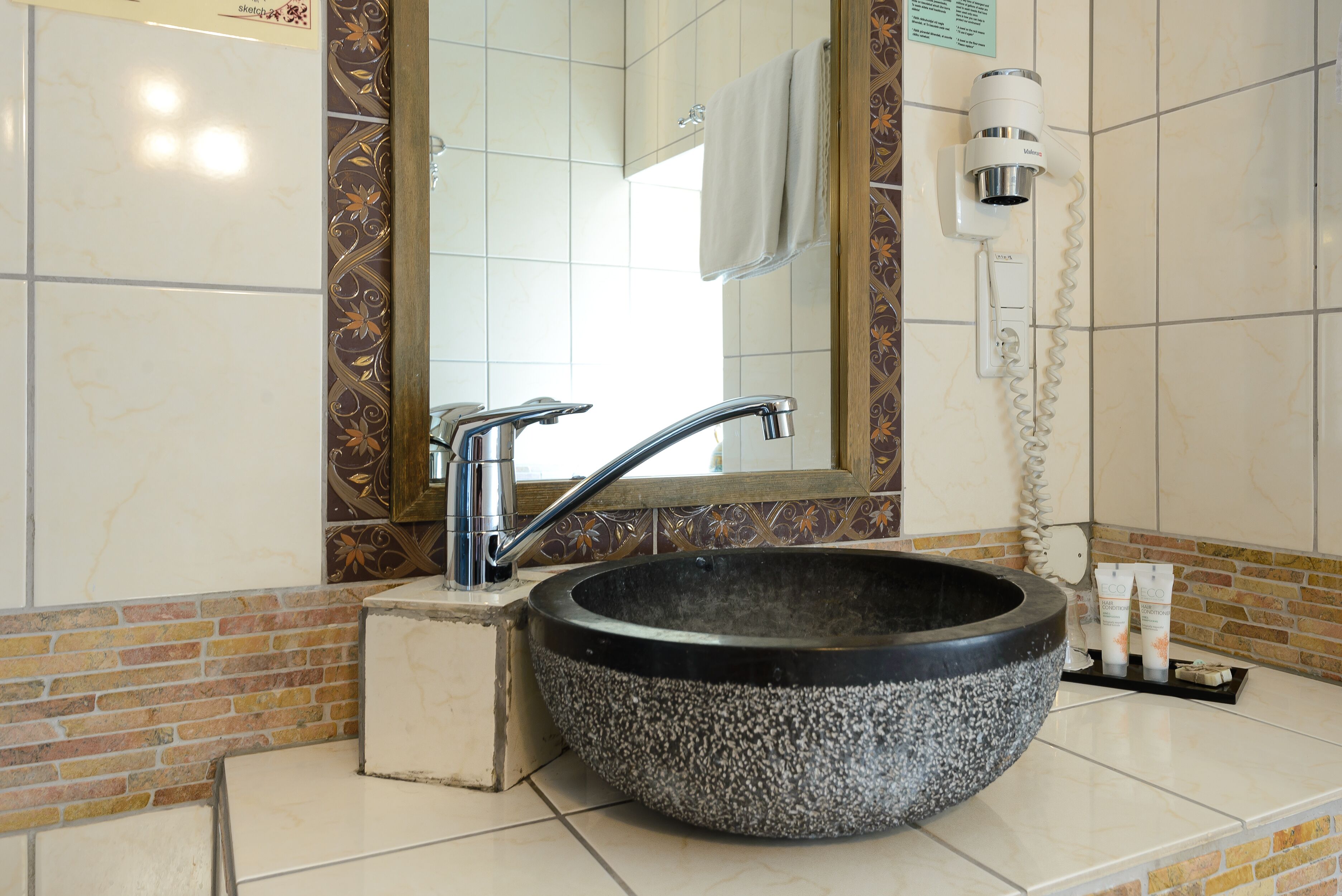 A bathroom with a large stone sink, a mirror, a towel rack, and a hairdryer.