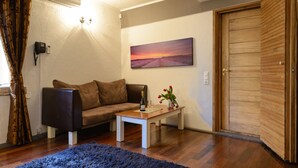 A living room with a brown sofa, a wooden coffee table, a painting of a sunset, and a wooden door. - Hotel Hansalinn (Parnu)