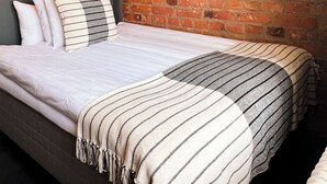 Un dormitorio con pared de ladrillo, una cama con ropa de cama a rayas, dos lámparas de pared y un cuadro enmarcado.