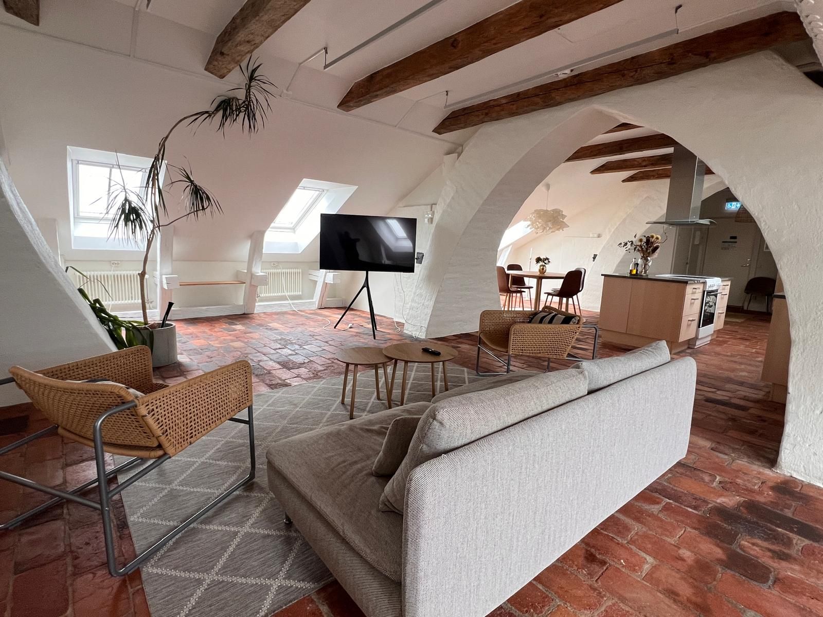 A loft-style living space with a sofa, chairs, a TV, and a dining area.