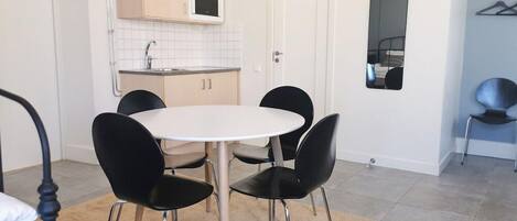 A compact kitchen with a white countertop, a microwave, and a sink. There is a round table with four chairs and a beige rug on the floor.