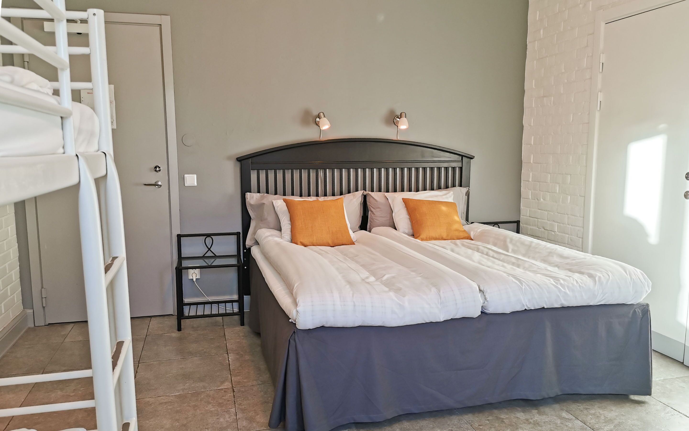 A bedroom with a bed, a nightstand, a ladder, and a brick wall.