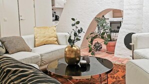 Un salón moderno con un sofá blanco, una mesa de centro redonda y un cojín estampado con motivos de cebra. Se aprecia una pared blanca con un clavo para llaves y una planta en maceta.
